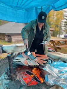 Ingela D, projektledare står vid elden och steker fisk.